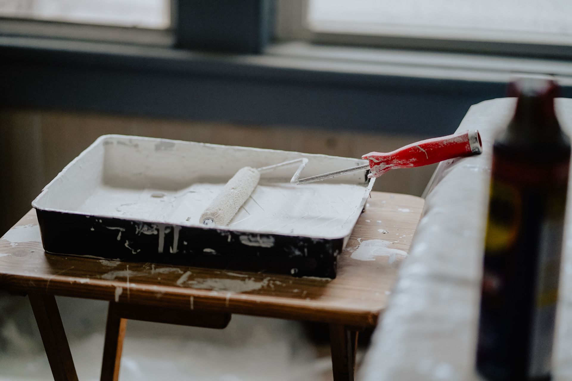 A paint roller and tray with white paint on a wooden table, indicating a renovation work.