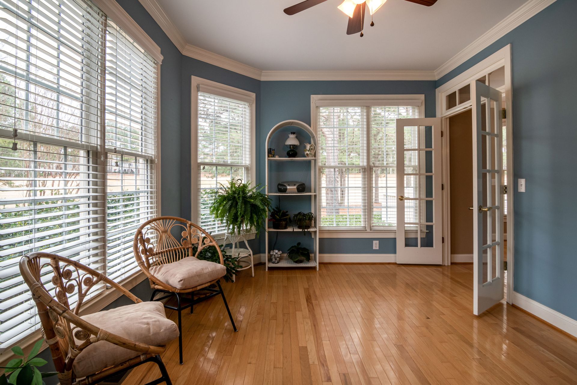 Bright and inviting room with wooden flooring, rattan chairs, and natural lighting through large windows.