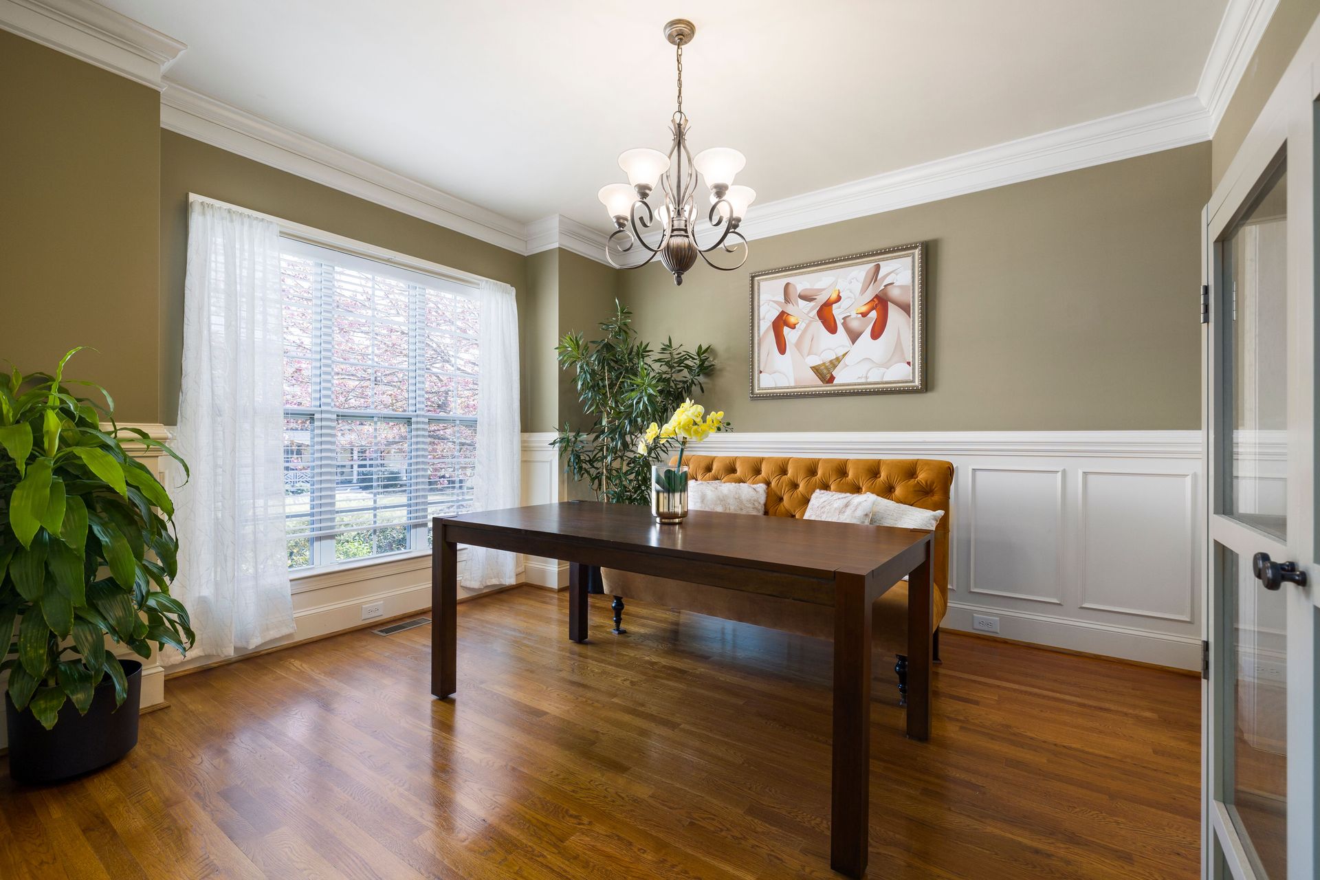 Cozy dining room featuring a chandelier, painting, and natural light through large windows.